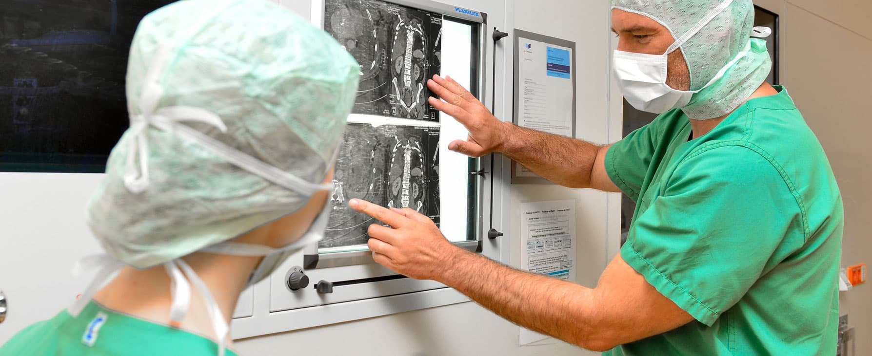Ein Chirurg in OP-Kleidung demonstriert einer Chirurgin Röntgenbilder