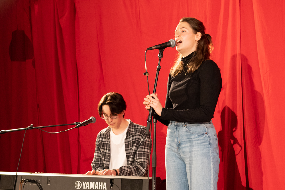 Die Sängerin steht am Mikrofon, links neben ihr sitzt ein junger Mann am E-Piano.