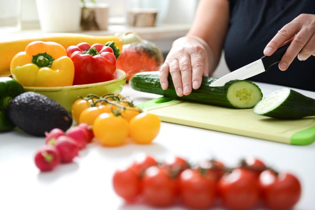 Eine Person die am Tisch mit einem Messer Gemüse schneidet.