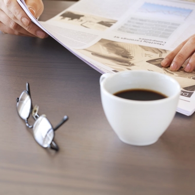 Zeitung, Kaffeetasse und Brille auf einem Tisch liegend