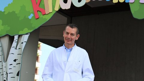 Professor Dr. Christian Kratz is standing in front of the entrance to the children's hospital.