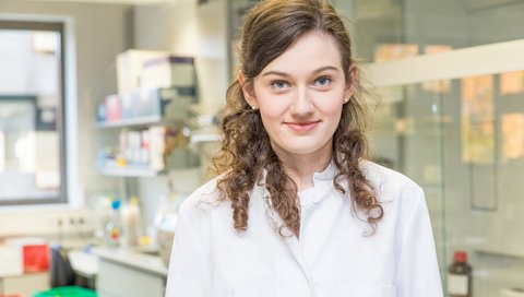 Laura Hinze stands in an MHH laboratory and smiles at the camera