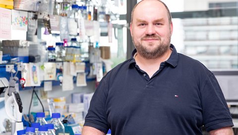  Portrait picture of Christoph Garbers standing in a laboratory room with various devices in the background. 