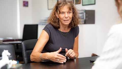 Professorin Hilfiker-Kleiner sitzt an einem Schreibtisch und spricht mit einer Person ihr gegenüber
