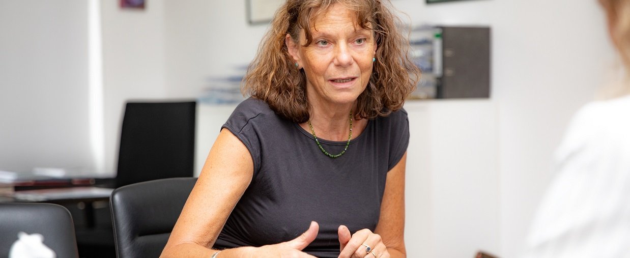 Professorin Hilfiker-Kleiner sitzt am Schreibtisch und spricht mit einer Person ihr gegenüber