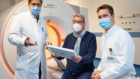 Professor Dr. Jens Vogel-Claussen, Patient Gerhard Lunow und Dr. Benjamin Bollmann stehen nebeneinander vor dem CT-Gerät im HANSE-Studien-Truck. 