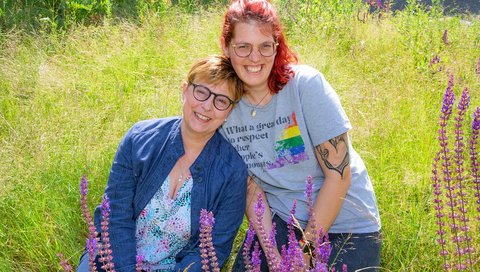Susanne Klyk and Anjan Pengel are sitting next to each other on a green meadow.