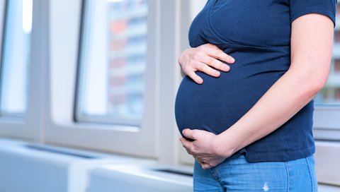 eine schwangere Frau umfasst ihren Bauch