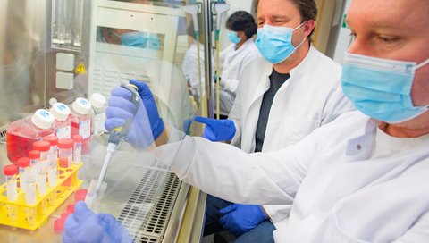 Professor Dr. Dr. Axel Schambach sitzt an einer biologischen Werkbank und schaut einem Mitarbeiter Dr. Marc Kleppa beim Pipettieren zu. 