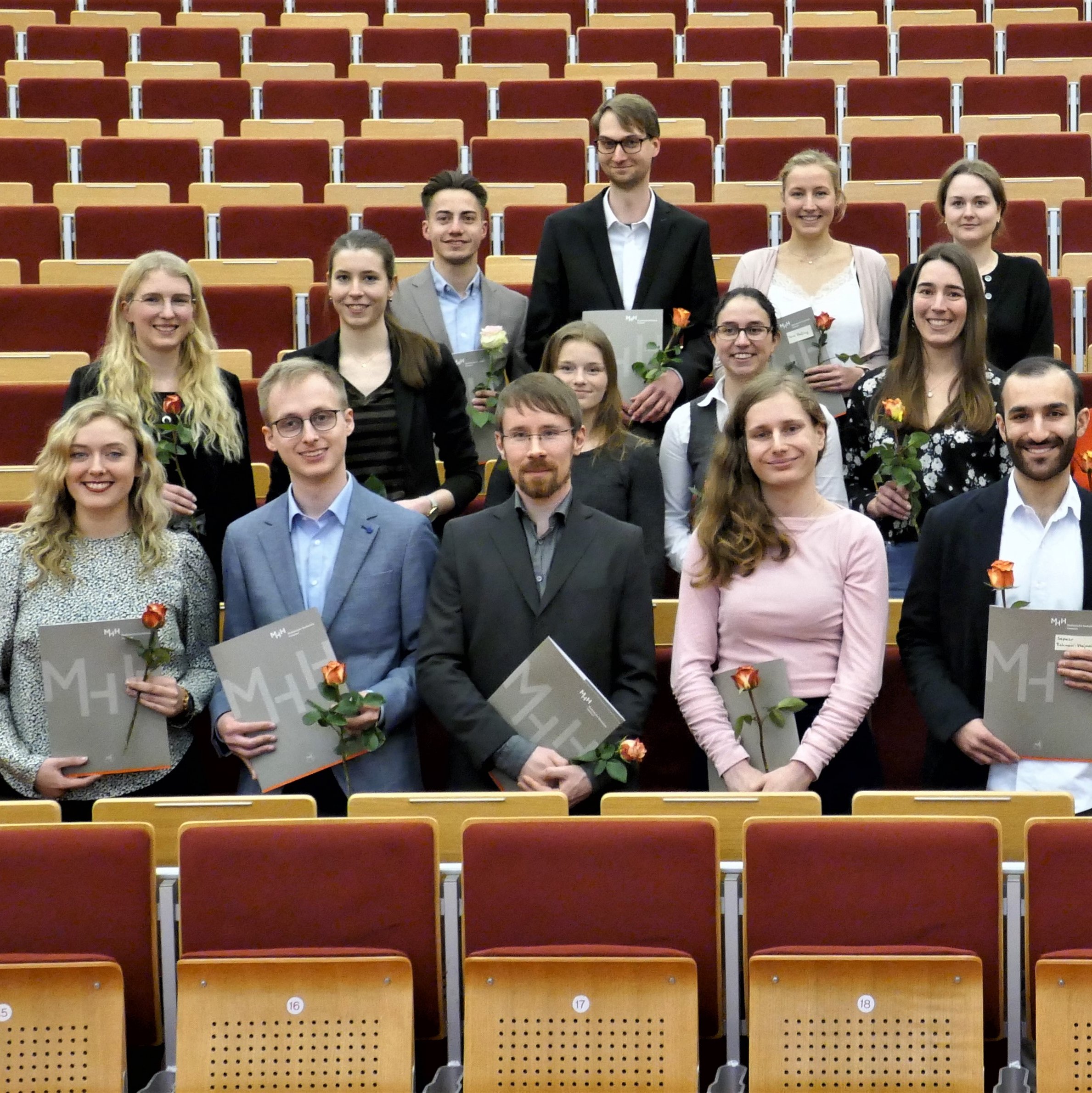 Mehrere Absolvent:innen stehen nebeneinander in einem Hörsaal der MHH und halten ihre Abschlussurkunden in den Händen. 