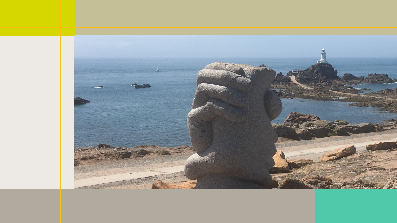 Das Bild ist an einem felsigen Strand aufgenommen. Im Vordergrund steht eine massive Steinskulptur, die zwei ineinandergreifende Hände zeigt. Im hintergrund steht ein kleiner weißer Leuchtturm in Ufernähe. Ein Fußweg fürhrt über aus dem Wasser ragende Felsen dorthin. 