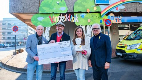 Frederike Ludwig-Lück, Peter Klein, Nils Meyer und Jörg Henschel stehen vor dem Haupteingang der MHH-Kinderklinik und halten eine symbolischen Check in den Händen sowie einen der Avatare, die mit dem Geld finanziert werden. 