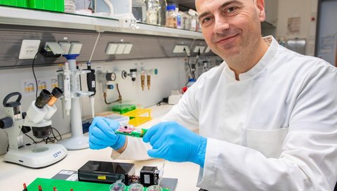 Ein Mann im weißen Kittel sitzt in einem Forschungslabor vor einem Untersuchungsaufbau für lebende Herzschnitte. 