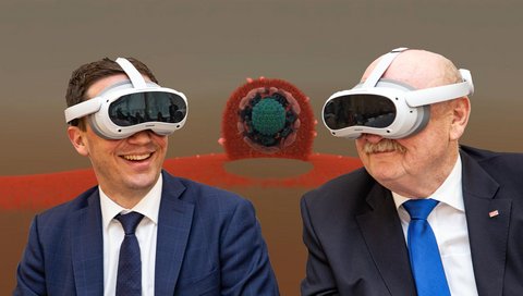 Minister Falko Mohrs und MHH-Präsident Professor Michael Manns tragen VR-Brillen und schauen sich einen Virtual Reality Film über das Lippenherpes-Virus an. Das Virus ist im Hintergrund schematisch dargestellt.
