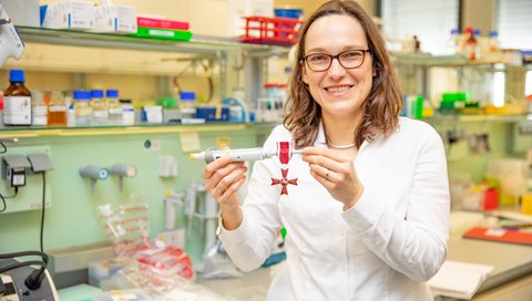 Professor Dr Alexandra Dopfer-Jablonka stands in the laboratory holding the Lower Saxony State Cross of Merit on a pipette.