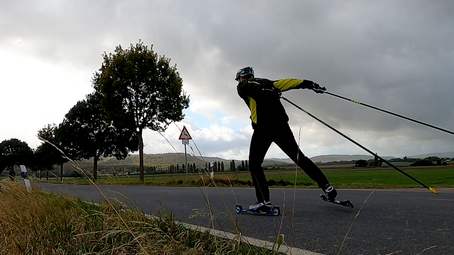 Ein Rollskifahrer gleitet vor einem wolkenverhangenen Himmel auf einer Landstraße dahin.