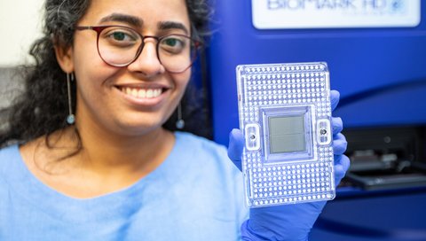 A woman in a blue lab coat holds a sample plate for genetic testing.