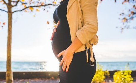 Copyright: Pexels/Pixabay_a pregnant woman in front of assumably a lake. On the left is a tree and some bushes. The woman holds her right hand between her breast and the beginnings of her belly. The left hand lies on her left groin.
