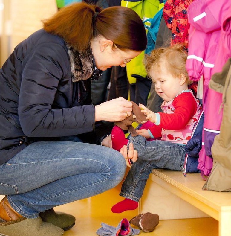 Eine Frau kniet vor einem Kind und zieht ihm die Schuhe an. 