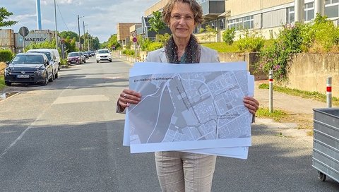 Martina Saurin stands on the Stadtfelddamm at the MHH campus and holds a map with the possible routes in both hands.