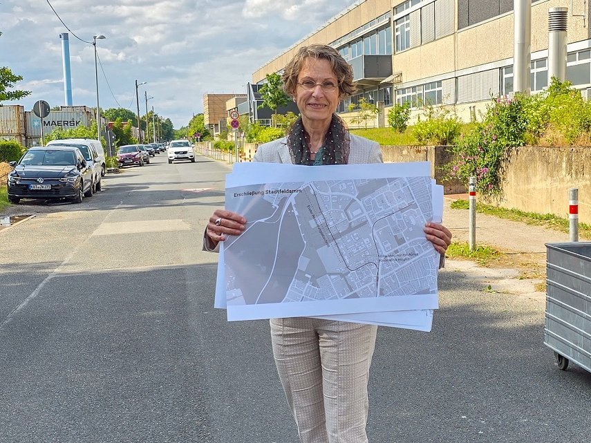 Martina Saurin stands on the Stadtfelddamm at the MHH campus and holds a map with the possible routes in both hands.