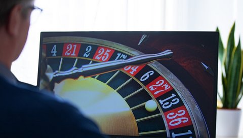 A man is sitting in front of a screen playing online roulette.