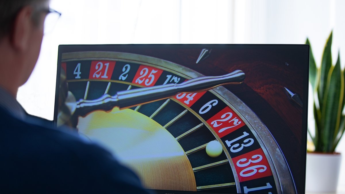 A man is sitting in front of a screen playing online roulette.