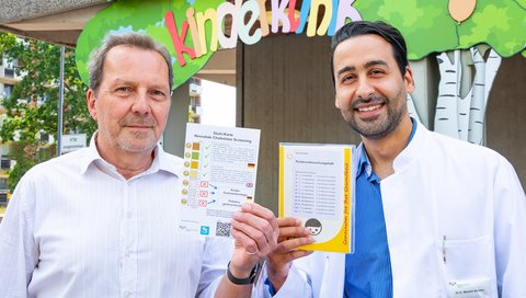 A doctor holds a stool colour chart in his hand, a second doctor the Yellow Booklet, in which the chart will be integrated in the future.