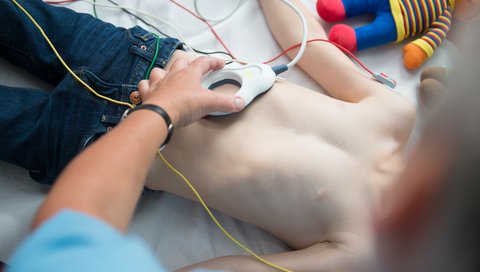 Verkabelter Oberkörper eines Jungen im Bett. Der Junge wird von einer Ärztin untersucht.