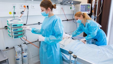 zwei weibliche Pflegekräfte stehen an einem Krankenbett
