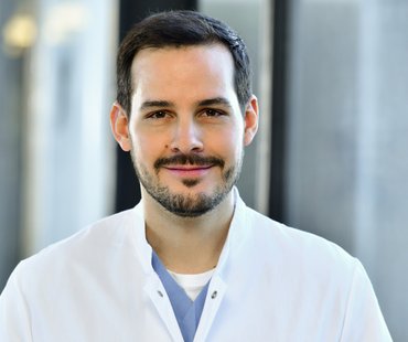 Porträtbild von Timo Hellms, der einen weißen Arztkittel trägt. 