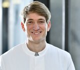 Porträtbild von Niklas Hoff, der einen weißen Arztkittel trägt.