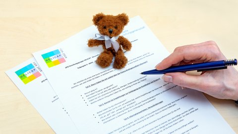 Ein kleiner brauner Teddy sitzt auf einem Fragebogen. 