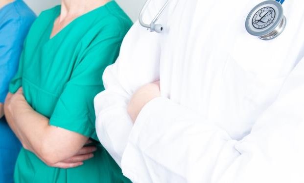 Copyright: medJUNGE Drei medizinische Fachkräfte stehen nebeneinander und verschränken entschlossen die Arme. Zu sehen ist nur der Bereich Schulter bis Bauchnabel.