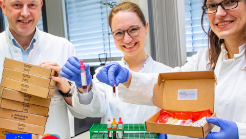 [Translate to Englisch:] Professor Dr. Georg Behrens, die Doktorandin Anne Cossmann (Mitte) und Professorin Dr. Alexandra Dopfer-Jablonka präsentieren Versandboxen und Blutentnahmeröhrchen.