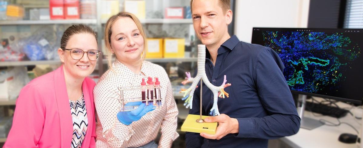 Eine Naturwissenschaftlerin, eine Ärztin und ein Arzt stehen in einem Labor und halten ein Lungenmodell und Blutproben in den Händen.