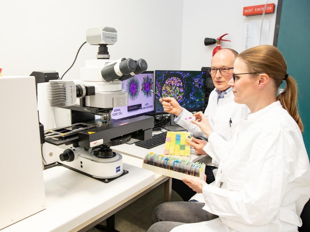 Ein Wissenschaftler und eine Wissenschaftlerin sitzen vor einem High-Tech-Mikroskop.