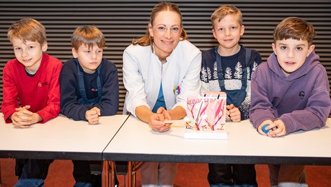 Dr. Eva Moennig umringt von vier Kinder bei der KinderUni-Vorlesung im Hörsaal F.