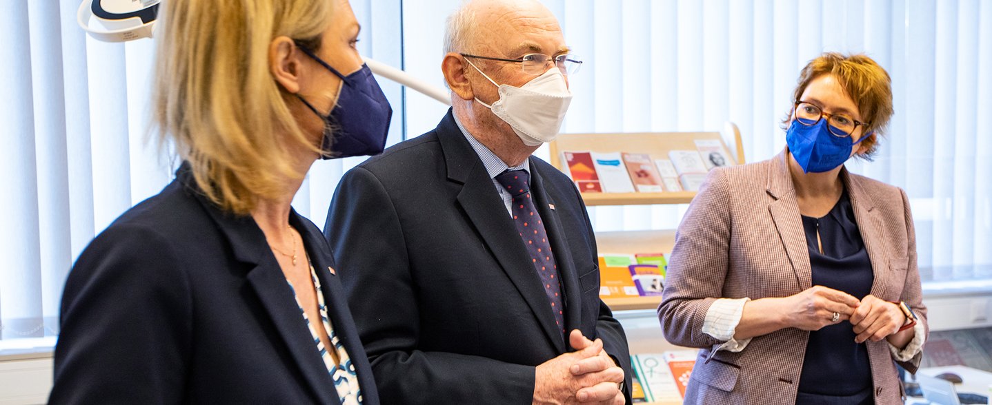 Prof. Dr. Anette Debertin, die niedersächsische Sozialministerin Daniela Behrens und MHH-Präsident Prof. Michael Manns stehen nebeneinander mit Mund-Nasen-Schutz in einem Raum der Kinderschutzambulanz. 