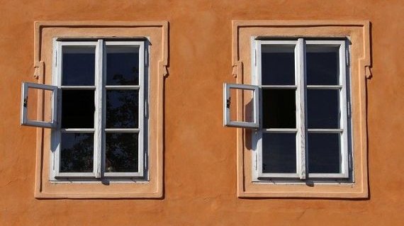 Eine braune, verputzte Hauswand mit zwei Sprossenfenstern, die nebeneinander liegen. Die Streben in den Fenstern teilen die Scheiben in je sechs kleine Quadrate auf. In beiden Fenstern ist das mittelere, linke Quadrat geöffnet. 