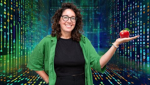 Eine Wissenschaftlerin steht in einem virtuellen Raum und hält einen Apfel in der Hand.