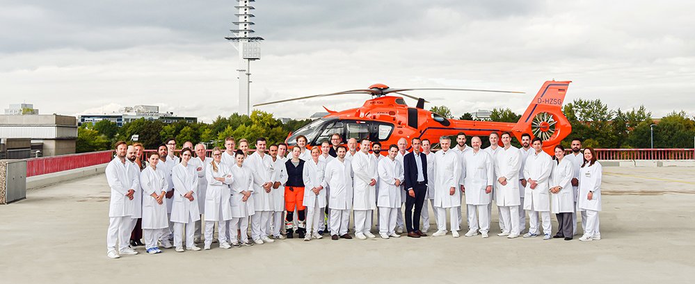 Das Team der Unfallchirurgischen Klinik der MHH steht vor dem Rettungshubschrauber Christoph 4 auf dem Landedeck der MHH. Im Hintergrund ist der Telemax zu sehen.