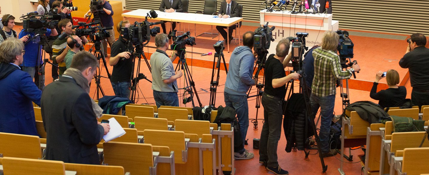 In einem MHH-Hörsaal stehen viele Journalisten und Kameras, die auf das Podium gerichtet sind. 