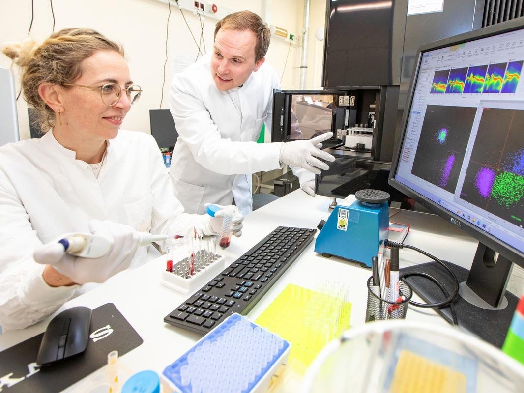 Ein Mann und eine Frau haben je einen Kittel an. Sie sind in einem Labor zu sehen an einem Bildschirm. 