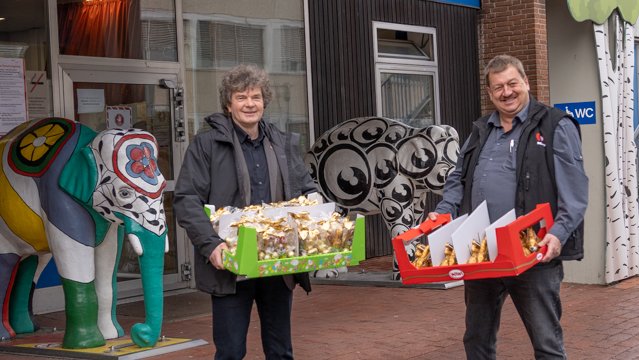 Dr. Schenke und Herr Brauckhoff stehen vor dem Eingang der Kinderklinik und halten beide einen Karton mit Schokohasen in den Händen.