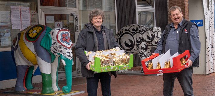 Dr. Schenke und Herr Brauckhoff stehen vor dem Eingang der Kinderklinik und halten beide einen Karton mit Schokohasen in den Händen.