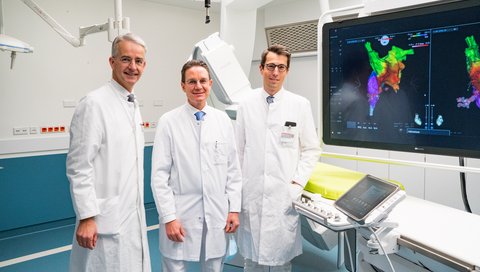 Professor Dr Frank Lammert, Vice-President of the MHH, Professor Dr Johann Bauersachs, Director of the Department of Cardiology and Angiology, and Professor Dr David Duncker, Head of the Hannover Heart Rhythm Centre, stand in the new electrophysiology laboratory. In the background are screens with colour 3-D images of the heart.