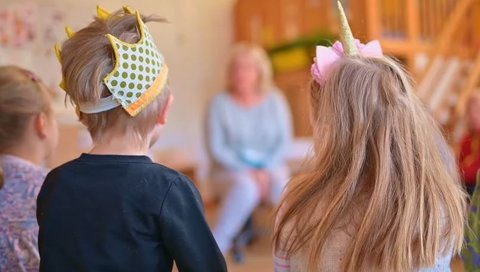 Mehrere Kinder sitzen in einem Stuhlkreis, einige tragen Kopfschmuck wie eine Krone aus Papier und einen Haarreifen mit Einhorn.