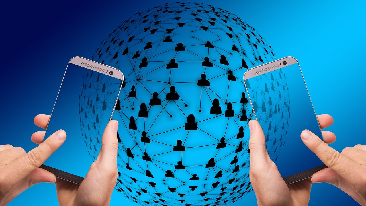Eine blaue Weltkugel, umspannt von einem Netz, an den Knotenpunkt sitzen Menschfiguren. Davor werden zwei Smartphones von Händen gehalten. 