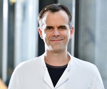 Porträtbild von Thomas Wirth, der einen weißen Arztkittel trägt. 